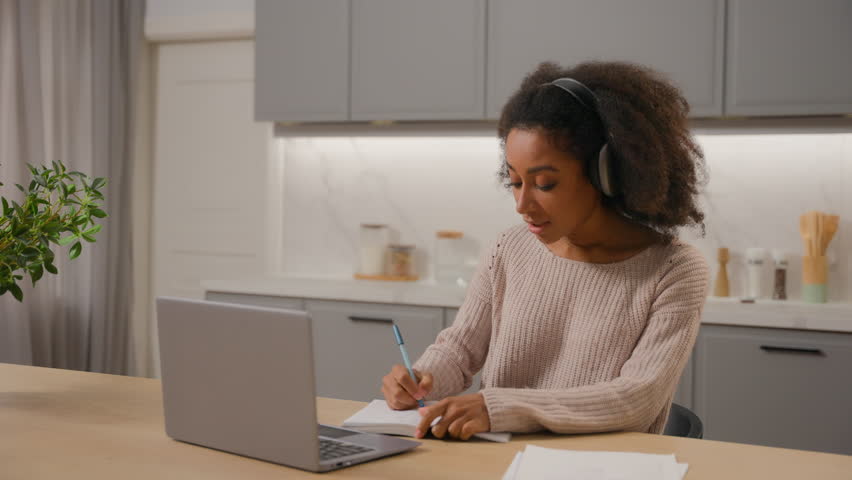 African American girl woman student schoolgirl learner studying online prepare for exam with laptop in home kitchen video call event class study e-learning in headphones writing tasks internet lesson Royalty-Free Stock Footage #3446746853