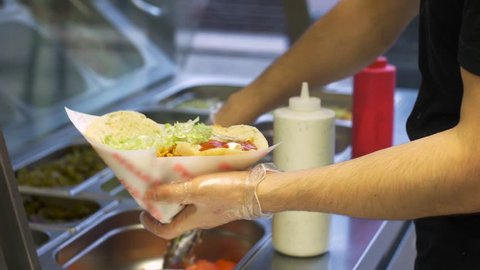 fast food and cooking concept - chef hands making pita with doner meat shavings and adding vegetables at kebab shop