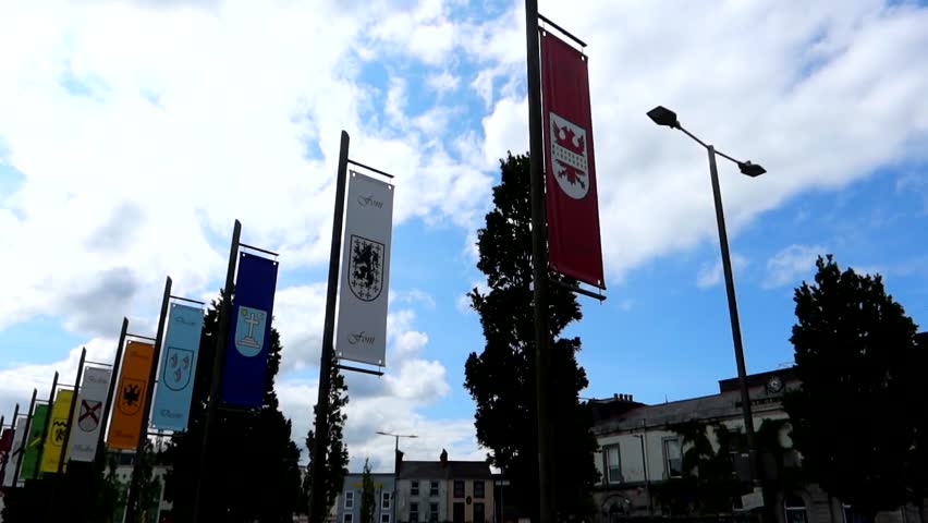 Galway , Ireland - 05 26 2023: Family Crest flags while people walk along Eyre Square