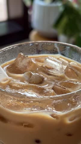 Pouring brewed coffee in a glass with ice cubes. Making iced latte or iced tea. Refreshing summer iced coffee or iced tea drink.