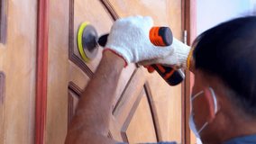 A middle-aged Asian man uses a wood sander to polish a door at home.