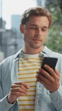 Vertical Portrait of a Handsome Young Man Wearing Casual Clothes and Using Smartphone on the Urban Street. Manager in Big City Connecting with People Online, Messaging and Browsing Internet.