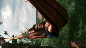 Relax in hammock. Carefree man lying in hammock and eating apple. Male relaxing in hammock in countryside. Vertical video