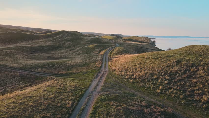 A beautiful aerial view. A worn winding pathway in the dunes. Sunset across a country track. Flying over the road along the shore