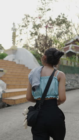 Asian brunette woman walks towards religious statue