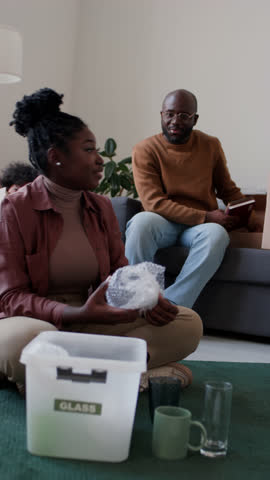Vertical shot of African American woman packing glassware with bubble wrap and speaking with husband while getting ready for moving Royalty-Free Stock Footage #3446946329