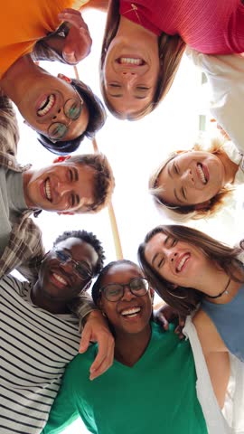 Vertical low angle view of a group of multiracial friends standing on a circle, smiling and embracing together. Young teenagers laughing and looking at camera. Team of people on a coaching meeting Royalty-Free Stock Footage #3446998489