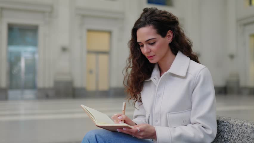 Young beautiful woman writing on notebook while sitting at train station. Travel and business people lifestyle concept.