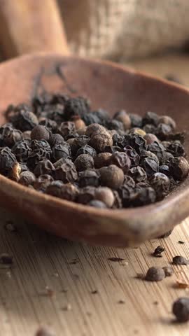 Vertical video. Slow motion of black peppercorns giving way on a wooden board