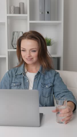 In this video, a cozy corner of the home is transformed into a health oasis where a woman focused on her computer takes a break to drink water, which gives her energy and positive attitude for the day