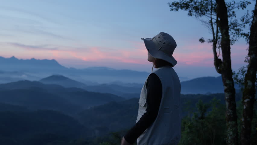 Asian happy tourist admire the mountainside scenery with hat and casual clothes and she smiles with her arms outstretched, enjoying nature. summer vacation trip on annual holiday, sun rises in morning Royalty-Free Stock Footage #3447125403