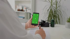 Doctor in hospital cabinet holding phone with green screen wearing white coat. Healthcare specialist in hospital cabinet using smartphone with mockup. - Powered by Shutterstock - Get 15% off with code: PIKWIZARD15