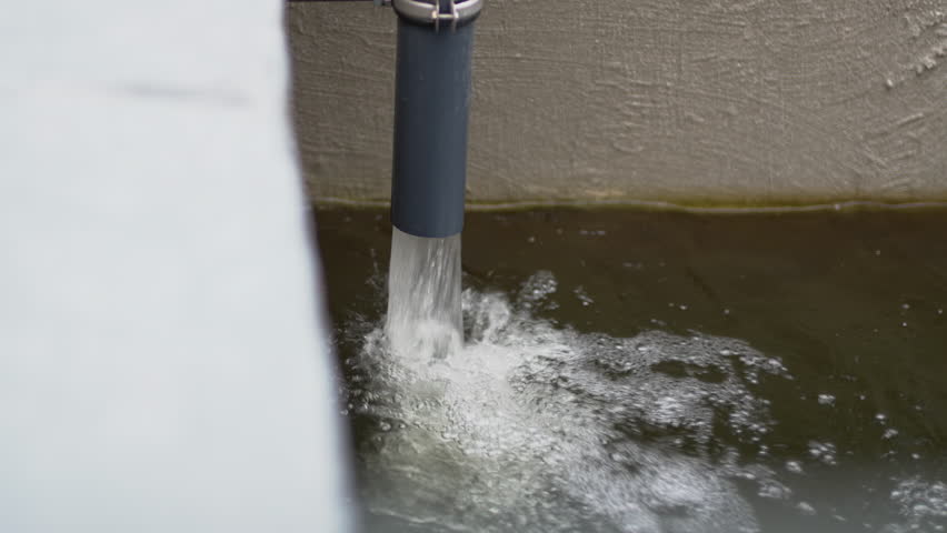 Running stream of treated water from pipe into storage basin closeup. Water undergoes temporary storage before releasing into environment