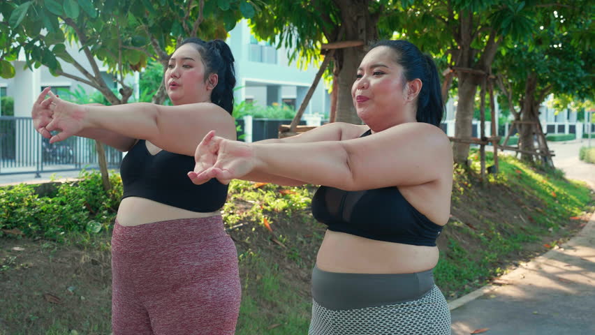 Obese two young asian woman doing stretching arm muscle in the park, woman with overweight warm up and exercise for dieting and health while handshake, oversized and workout, plus size. Royalty-Free Stock Footage #3447181911