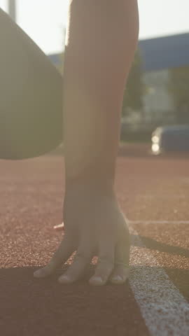 Caucasian woman at the athletic track starting point, hands on the start line and legs on starting block, ready set and go, handheld shot.