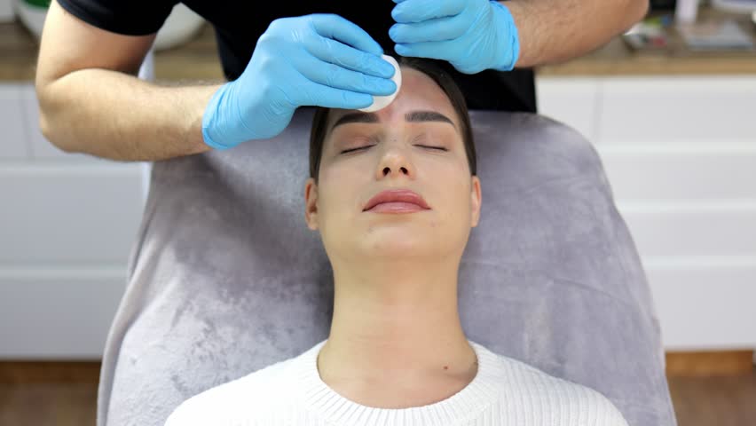 Close-up of a beautiful young woman undergoing a cosmetic procedure with a beautician and cleansing her face before an injection.