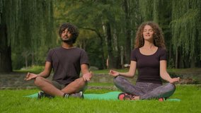 Yoga sport morning meditation multiracial couple Arabian Indian man Caucasian woman sit in lotus pose zen together meditate relaxing in park nature outdoors spiritual mindfulness peace balance in city - Powered by Shutterstock - Get 15% off with code: PIKWIZARD15
