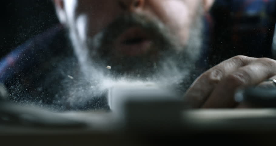 Super slow motion macro of artisan carpenter is blowing sawdust from woodwork after sanding it with hands and sand paper on workbench in workshop at 1000 fps.
