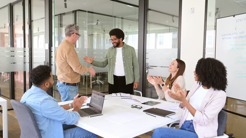 A team circles around a meeting table where a handshake between two members takes center stage, reflecting a moment of agreement or accomplishment within a diverse and cooperative workgroup Royalty-Free Stock Footage #3447269655