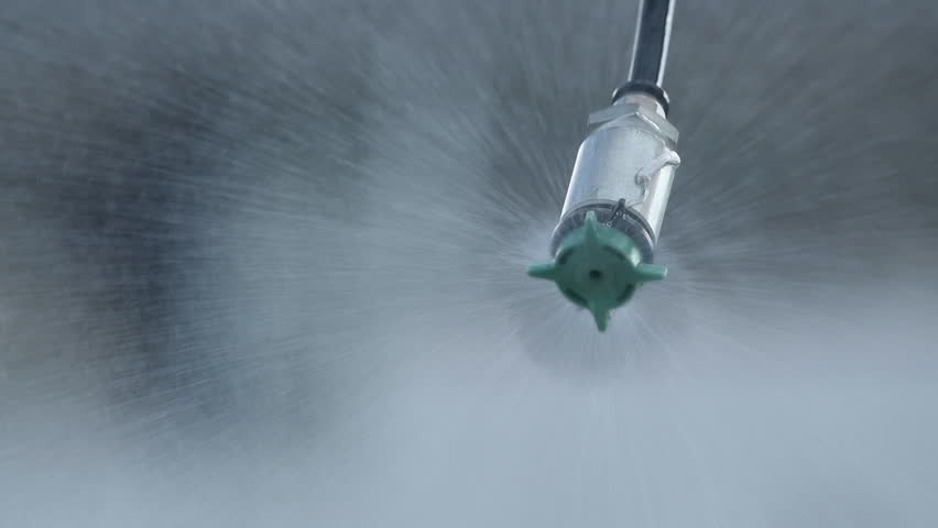 Closeup of agricultural sprinkler head spraying water drops at field, slow motion with selective focus