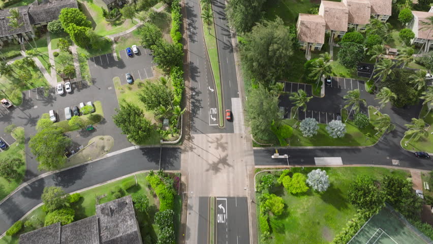 Red car driving by exclusive vacation residential property on sunny summer day. Summer cottages on green tropical island of North shore Oahu Hawaii. Aerial view of Kuilima drive leading to Turtle bay