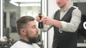 Moistening with water from a spray bottle before cutting with scissors. Caucasian bearded man having his hair sprayed by a barber.