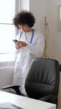 Young hispanic latin female doctor using mobile phone typing message at medical consultation. Technology and medicine concept. Vertical video.