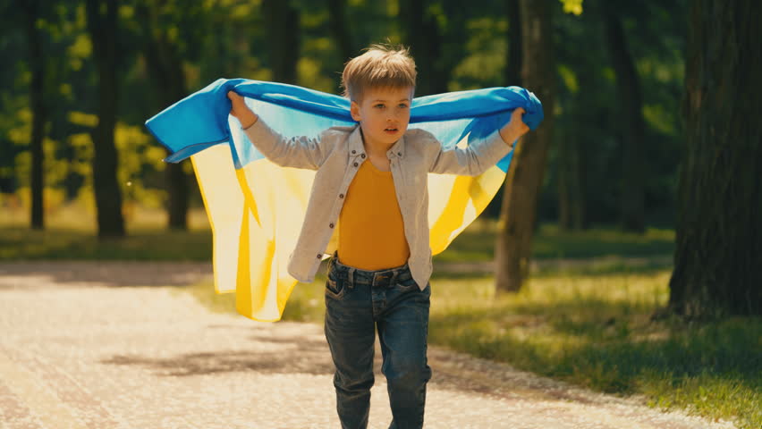 Joyful child with flag of Ukraine running in summer park, proud little patriot