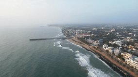 Drone footage approaching the city from the sea. The whole of Puducherry, an lighthouse, is visible in early morning aerial footage. The Bay of Bengal waves. Aerial video of the sea and the city.