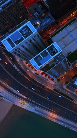 Quick cars moving by the highway at the waterfront. Drone flying high above the skyscrapers at the downtown Chicago. Vertical video.