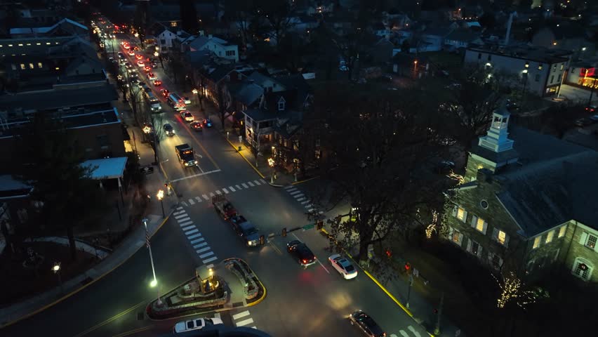 Small American town at night. Aerial drone flight above dark street with cars driving. Town square with American flag.