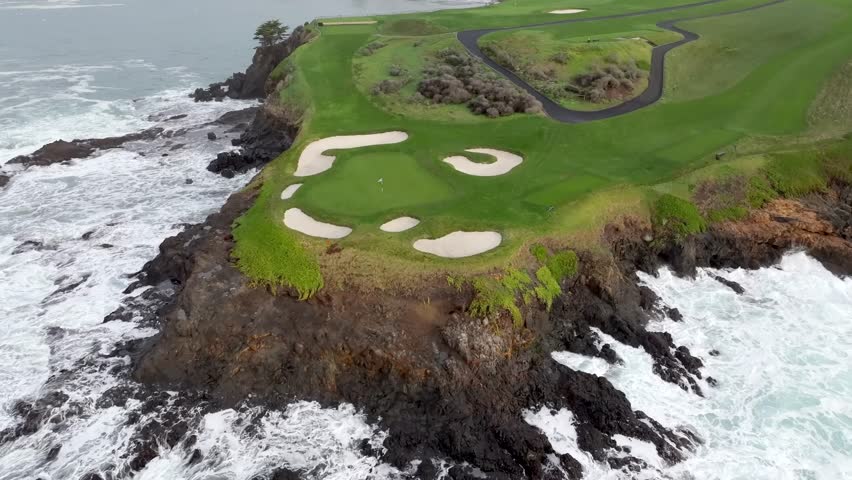 Pebble beach golf links with rugged coastline and crashing waves, aerial view