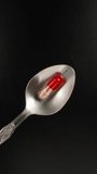 Red and white pill, capsule on a spoon, black background, top view. Dolly slider extreme close-up. Laowa Probe Vertical video.