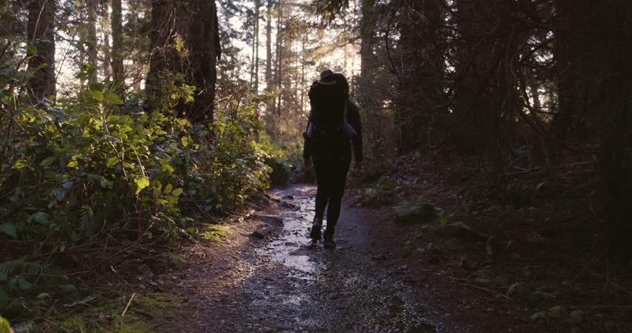 Mother and Baby Boy in backpack carrier hiking in the forest. Sunny sunset. Lighthouse park, West Vancouver, BC, Canada.