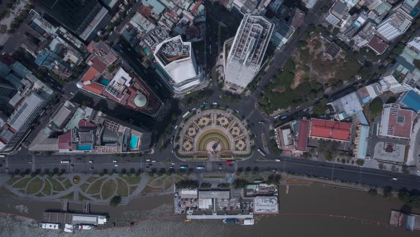 Saigon Vietnam traffic roundabout top down aerial hyperlapse. City buildings , park and ferry wharf can be seen. Establishing shot of Ho Chi Minh City center landmark on sunny clear day.