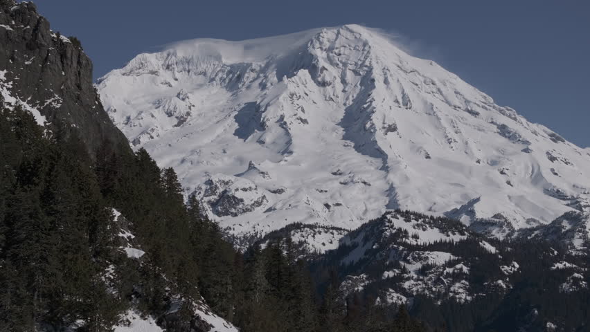 Ungraded aerial drone footage of Mount Rainier under light blue sky on a bright, sunny winter morning in Washington State.