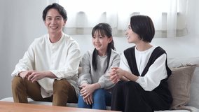 young asian family watching tv together sitting on sofa in living room
