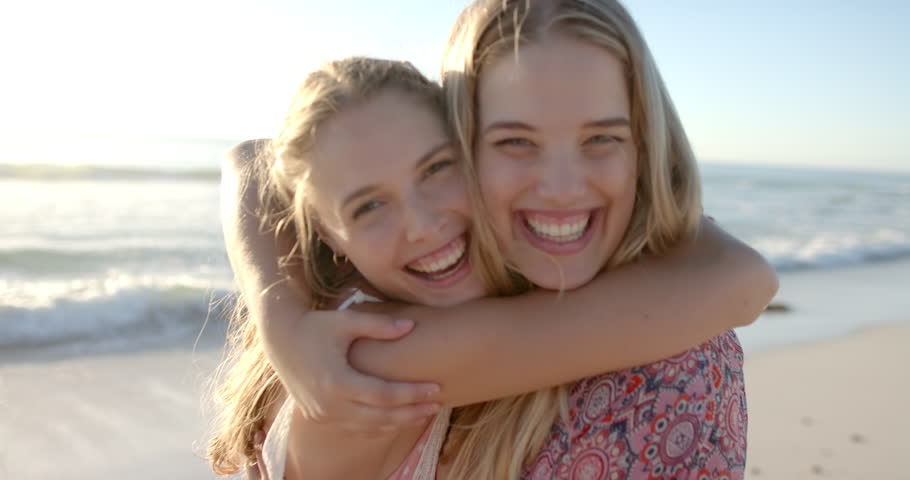 Two young Caucasian women embrace joyfully on a sunny beach. Their laughter and close bond are evident as they enjoy a carefree day outdoors, slow motion.