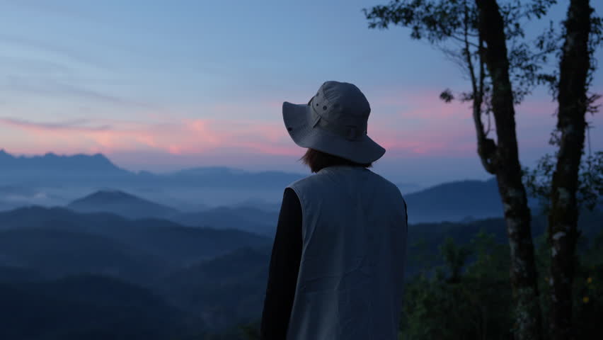 Asian happy tourist admire the mountainside scenery with hat and casual clothes and she smiles with her arms outstretched, enjoying nature. summer vacation trip on annual holiday, sun rises in morning Royalty-Free Stock Footage #3447501673