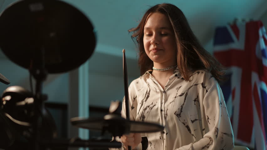 Slow motion. Close-up. A young girl musician smiles and laughs while playing an electronic drum kit, sitting in the studio of a music school