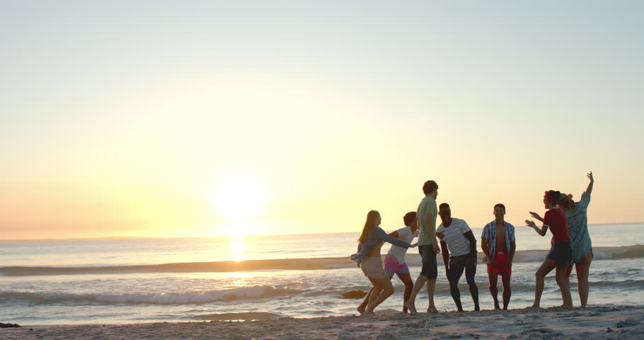 Diverse friends enjoy a beach at sunset, with copy space. The group's laughter and conversation add warmth to the serene outdoor setting, slow motion. Royalty-Free Stock Footage #3447522471