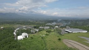 Aerial view of factory building on the rural Indonesia. Woking industry with chimney emits smoke from burning fossil fuels. air pollution