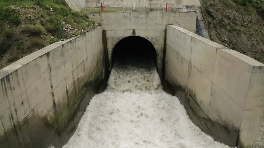 Forceful water gushing from a hydroelectric dam tunnel into a river channel with reinforced walls