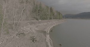 Ungraded wide-angle aerial drone footage of a rural mountain highway alongside a large fresh water lake surrounded by forests and mountains on a cloudy morning in Washington State.