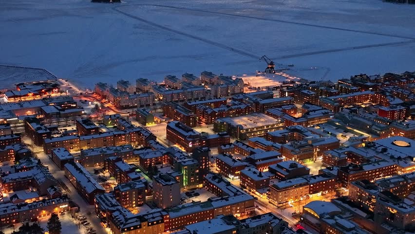 Twilight descends on snow-covered Luleå cityscape, glowing streetlights, aerial view Royalty-Free Stock Footage #3447663737