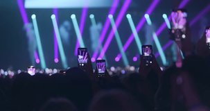 Fans film popular music band concert on phones, close up. Viewers crowd record bright neon light show for social media. Lot fun people enthusiastically take photos of music festival on smartphones