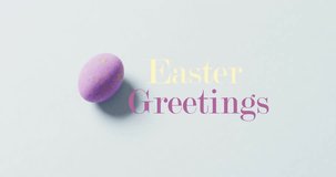 Animation of happy greetings text over purple easter egg on bue background. Easter, religion, christianity, tradition and celebration concept digitally generated video.