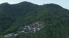 Drone shot of rural landscape with view of remote village on forested hills. Aerial view of tropical countryside in Indonesia.