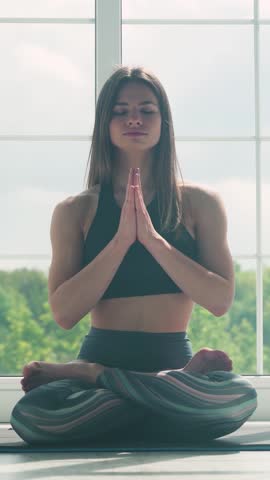 Young woman meditates and does yoga, a calm mood, relaxing in a white room filled with light, the girl is sitting on the floor, vertical video for social networks. Royalty-Free Stock Footage #3447717477