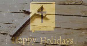 Animation of happy holidays text over christian cross on wooden background. Easter, religion, christianity, tradition and celebration concept digitally generated video.